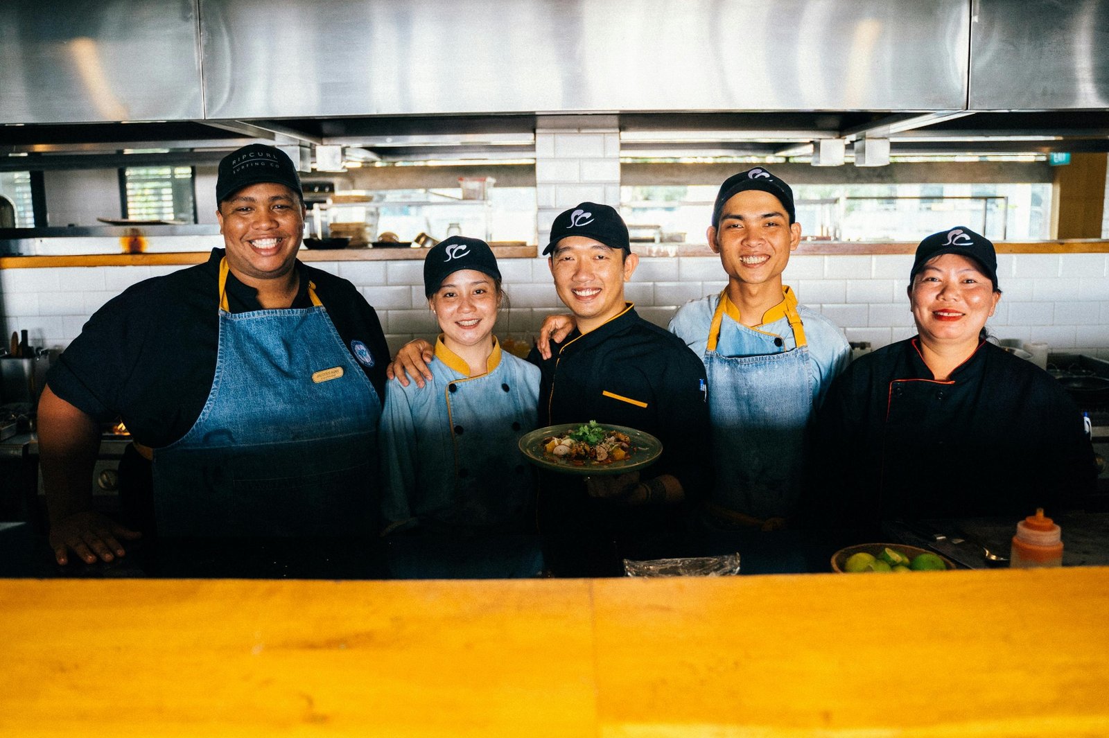 Restaurant kitchen team of chefs and line cooks smiling together while presenting a finished dish, showing how trained staff drive customer satisfaction and restaurant revenue growth