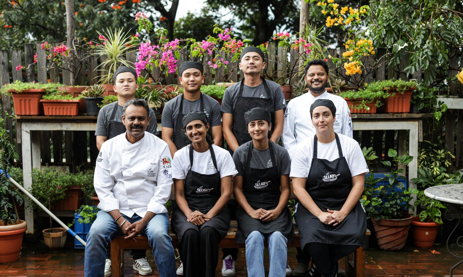 Restaurant team posing together in aprons and chef hats outside the kitchen