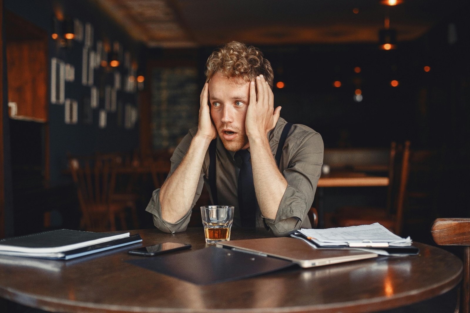 Stressed restaurant manager holding his head in his hands at a table covered with paperwork, phone, and tablet, overwhelmed by daily operations