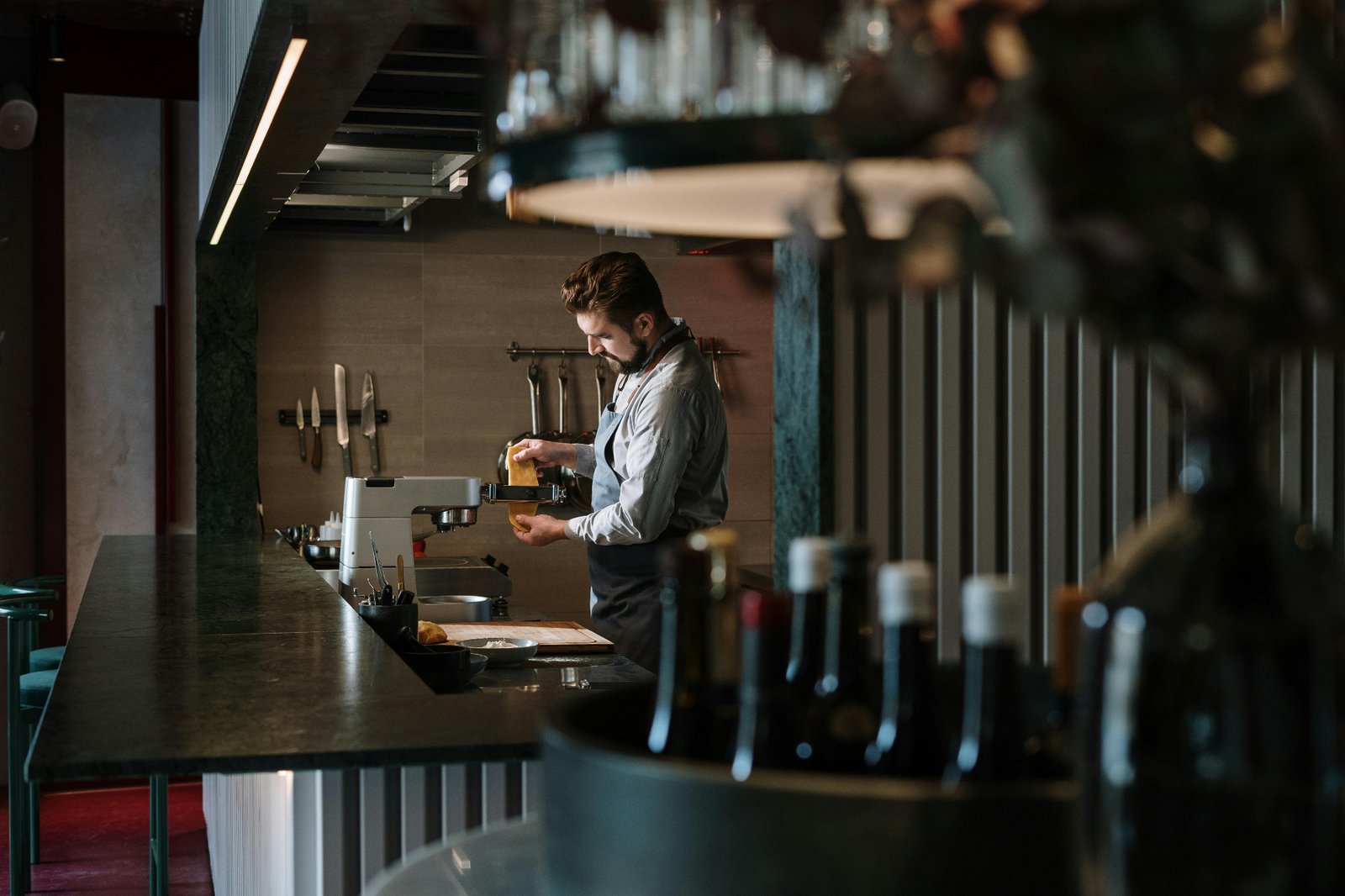 Chef preparing pasta in a modern open kitchen lined with knives and wine bottles