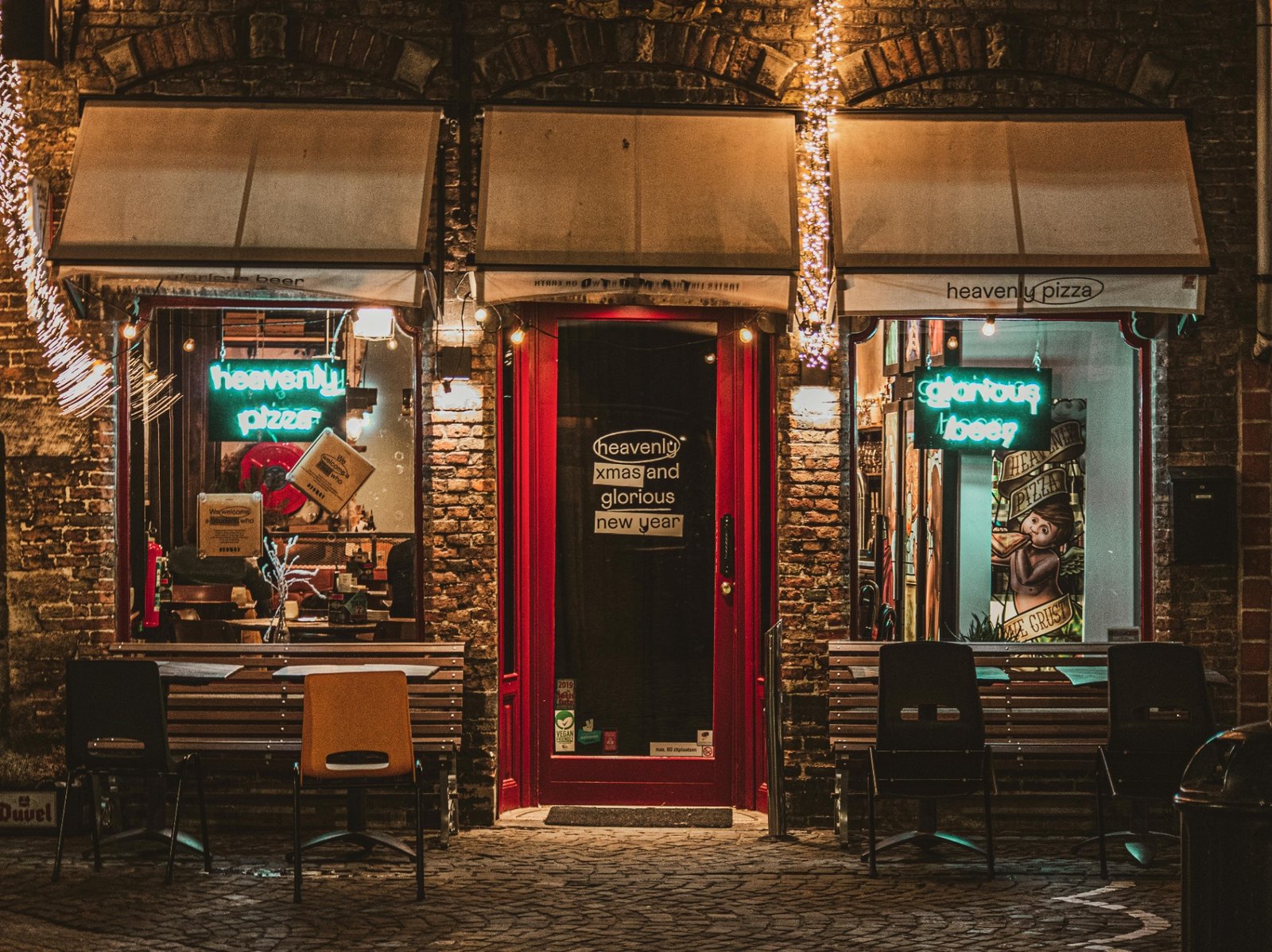 Independent neighborhood pizzeria storefront lit up at night with neon signs and outdoor seating