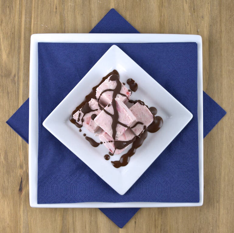 No-Churn Strawberry Ice Cream, cut in cubes on plate, drizzled with chocolate