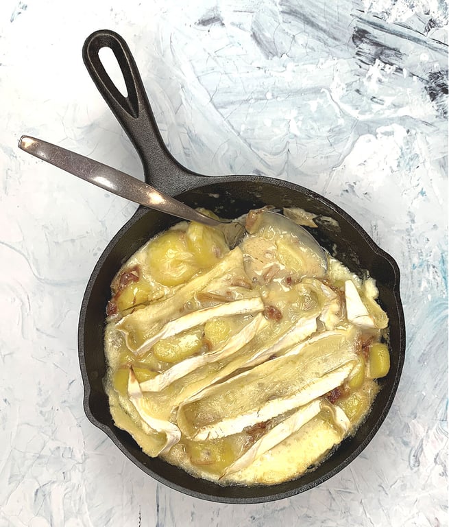 Cast-iron skillet with tartiflette just coming out of the oven with melted brie cheese.