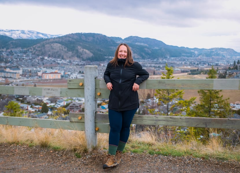 Woman leans against a wooden fence on a rainy day, wearing a black rain jacket.