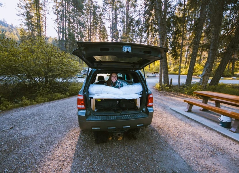 Woman lays in the back of a Ford Escape SUV converted for camping