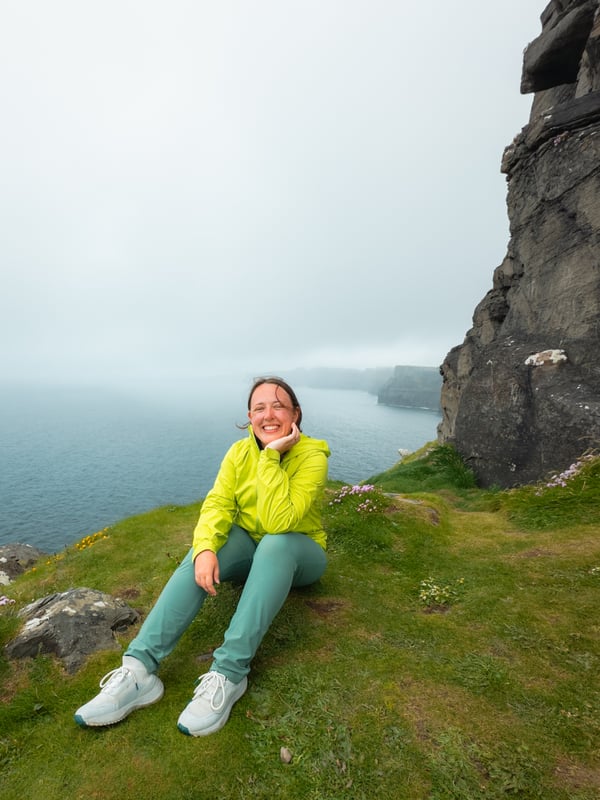 Woman poses for a photo with the Cliffs of Moher in the background on a misty day