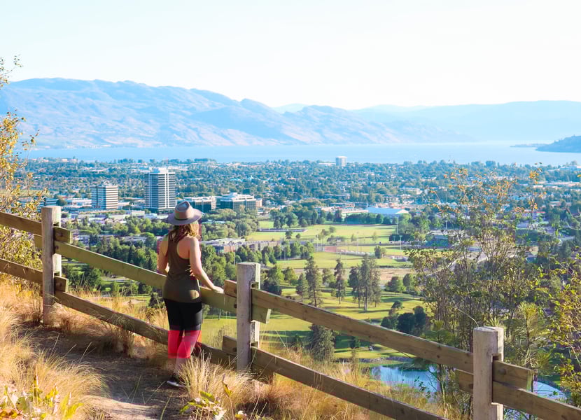 Woman standing near a wooden fence at Dilworth Mountain Park, overlooking Kelowna and towards Okanagan Lake