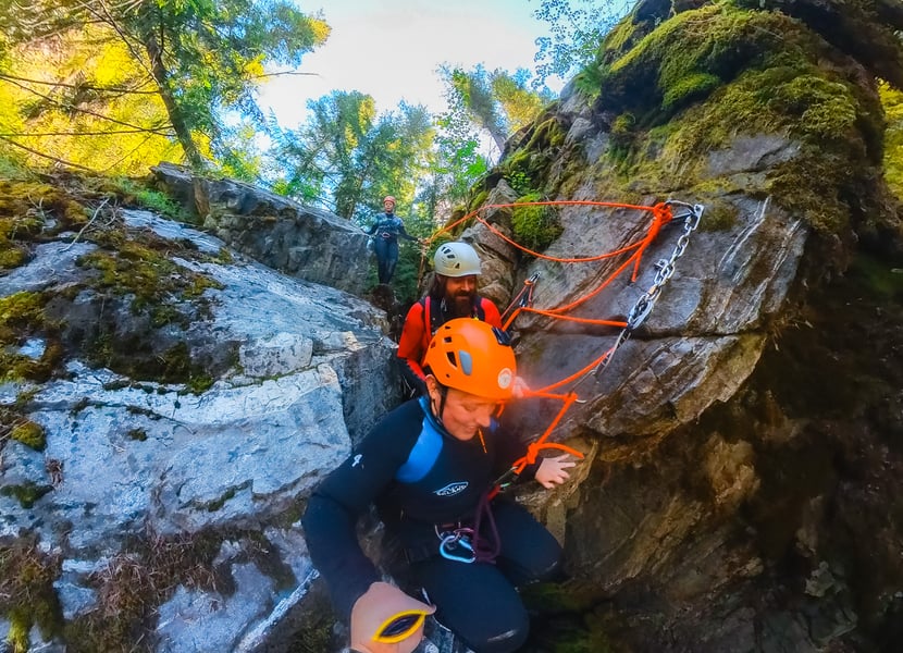 A trained canyoning guide helps a woman rappel down a waterfall