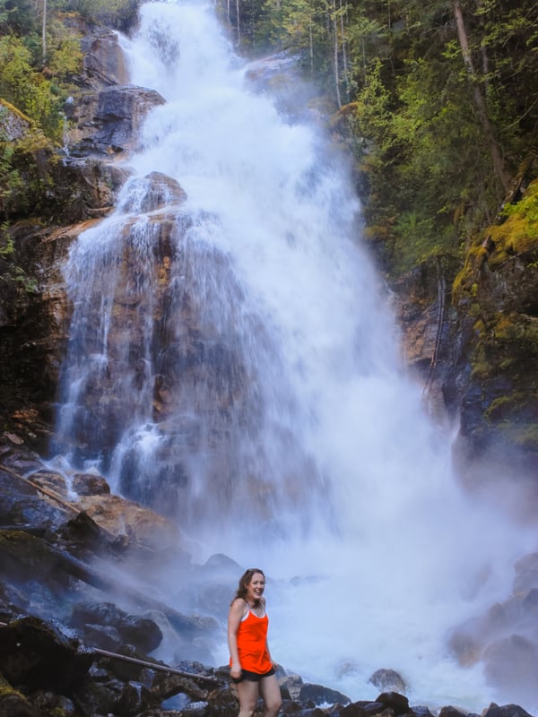 Woman in red stands in front of Kay Falls as it rushes down in the spring