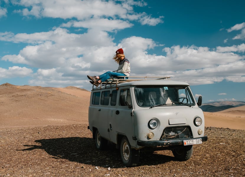 Woman sites on top of a vintage van while on a road trip.