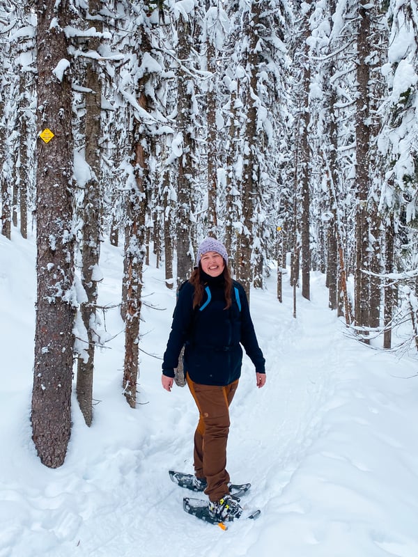 Woman in snowshoes on a snowy trail wearing a rain jacket as an outer layer.