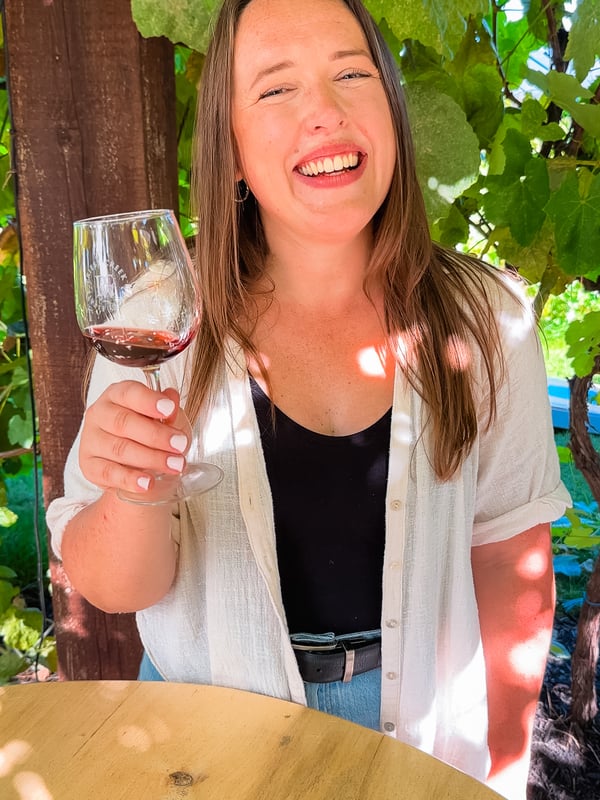 A woman smiling and holding a wine glass at Priest Creek Winery.