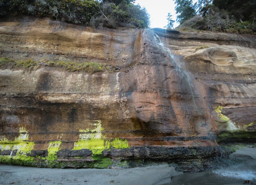 Trickle of the Mystic Beach waterfall flowing over rocks and into the ocean during low tide.