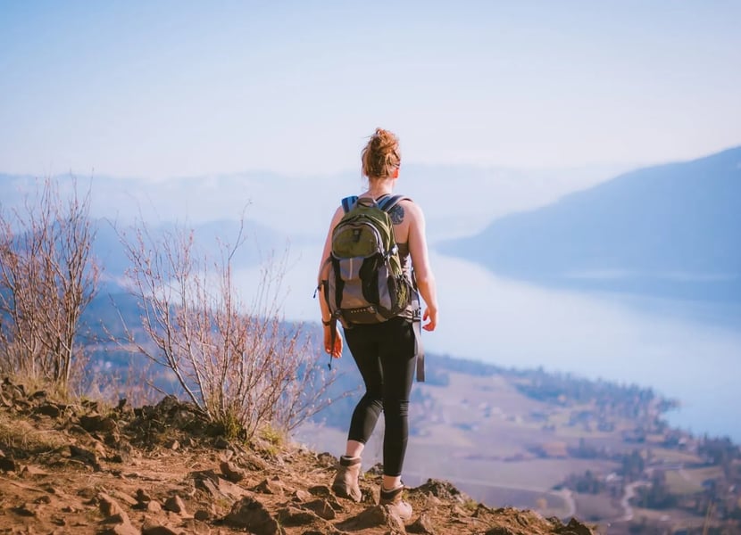 A woman stands at the top of a mountain, overlooking Okanagan lake.