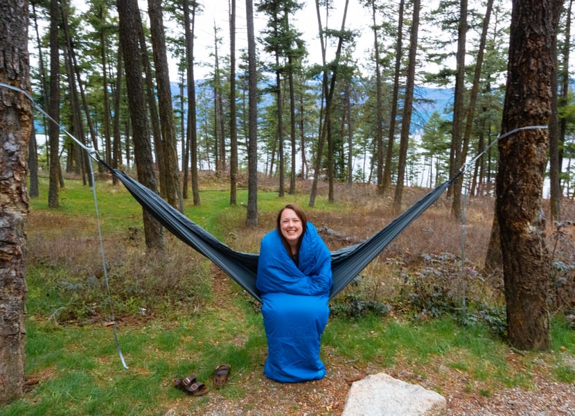 Woman sits on a hammock bundled in a sleeping bag