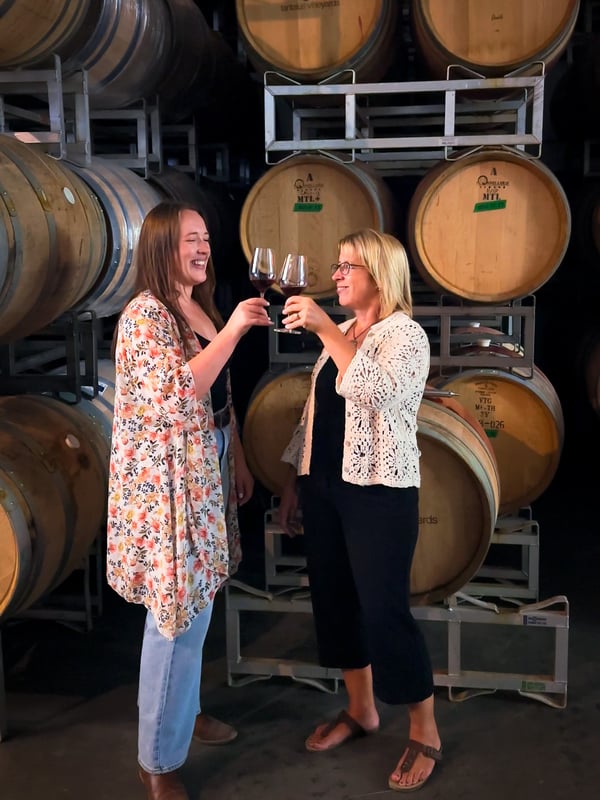 Two woman cheersing in front of wine barrels at Tantalus Vineyards in Kelowna.
