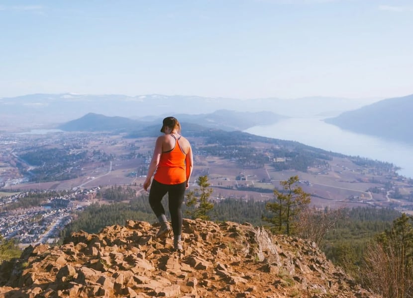 Woman standing at the top of Spion Kop hike overlooking Lake Country and Okanagan Lake.