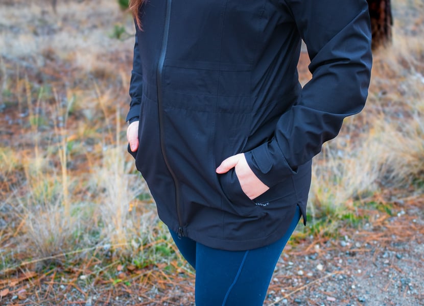 Woman with hands in pockets of a black rain jacket.