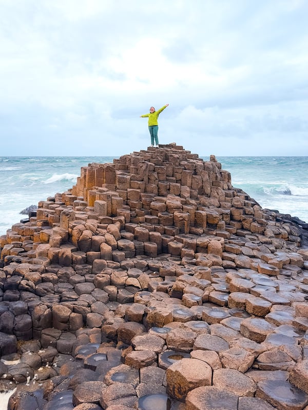 Woman in green standing with hands up on top of basalt columns at Giant's Causeway