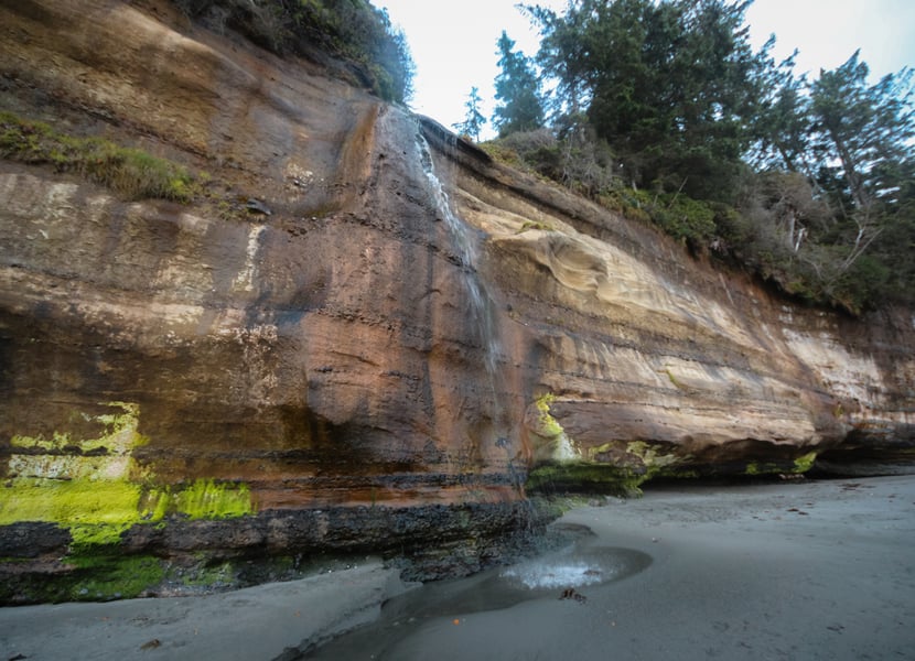 Trickle of the Mystic Beach waterfall flowing down the rocks and into the ocean, captured during low tide.