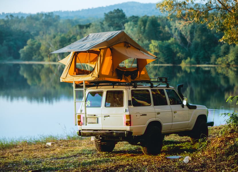 Rooftop tent on a jeep next to a lake.