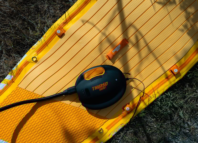 An electric paddleboard pump sitting on top of a yellow Waterwalker Thurso Surf paddleboard