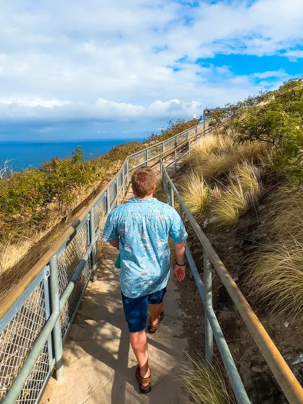 Man walking along a fenced and paved trail.