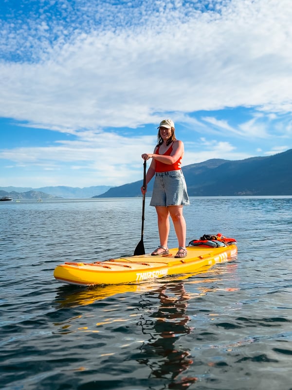 Woman standing on a yellow Thurso Surf paddleboard on a lake