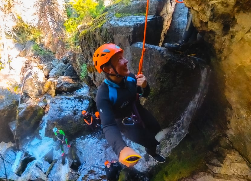A woman rappels down a waterfall in a canyon