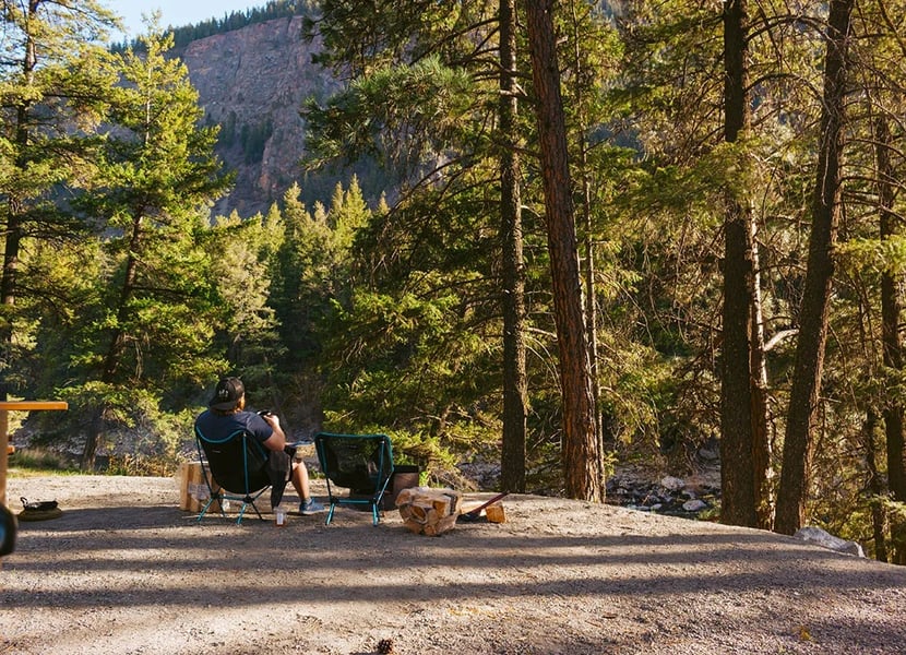Man sits on small camping chairs in a campsite in BC.