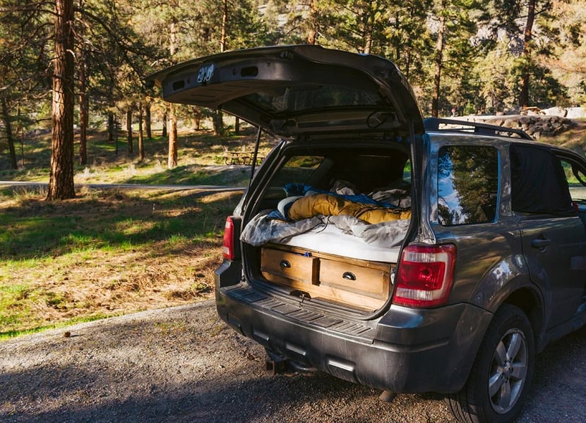 SUV with open hatch that's set up for car camping with blankets, pillows, and drawers