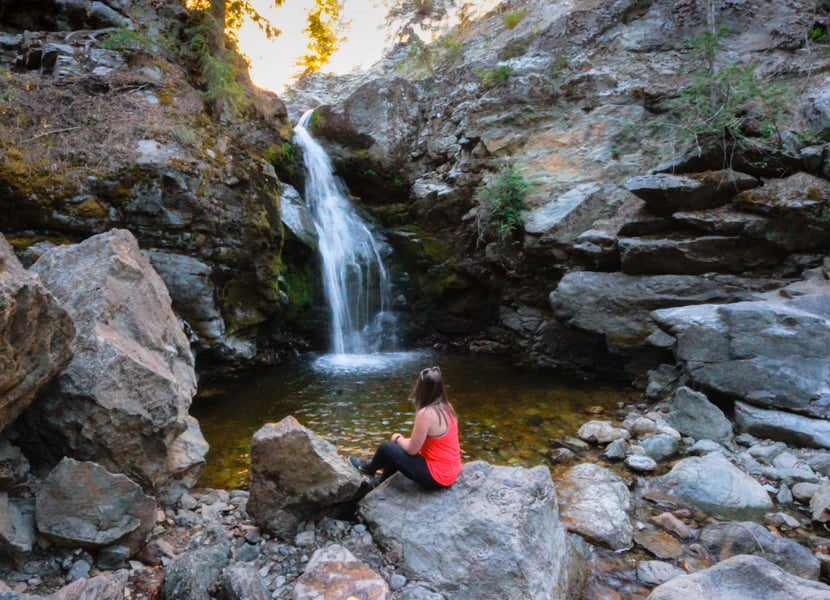 Woman in red sits in from of Canyon Falls in Kelowna