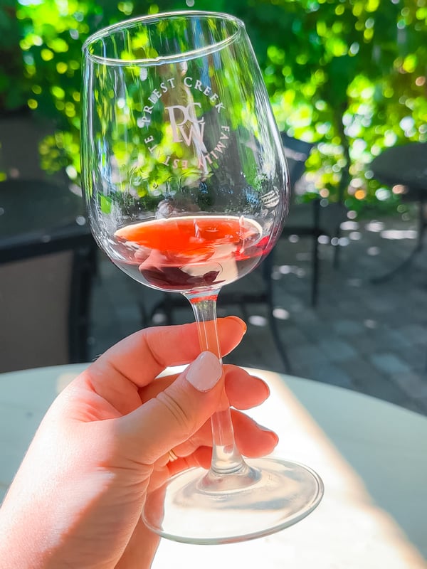 Woman holding a wine glass in front of a vine covered terrace at Priest Creek Winery in Kelowna.