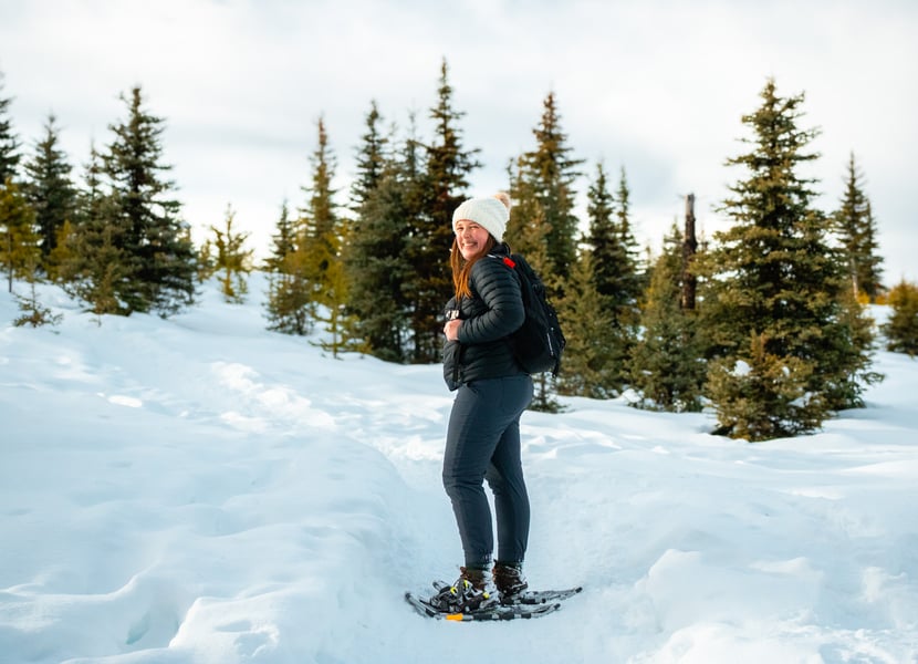 Woman snowshoeing on a sunny day through alpine trees in kelowna