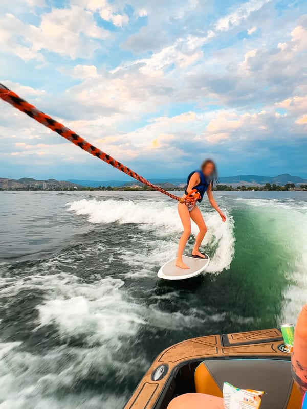 Woman wakesurfing on Okanagan Lake with Kelowna in the background.