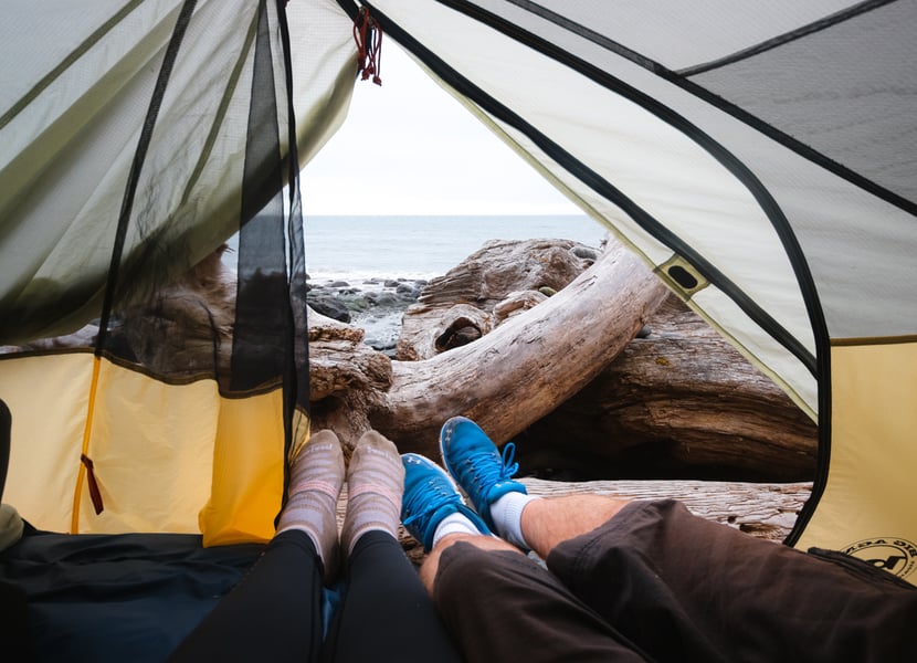 Feet inside a tent with the ocean and Mystic Beach visible in the background, showcasing a cozy camping setup