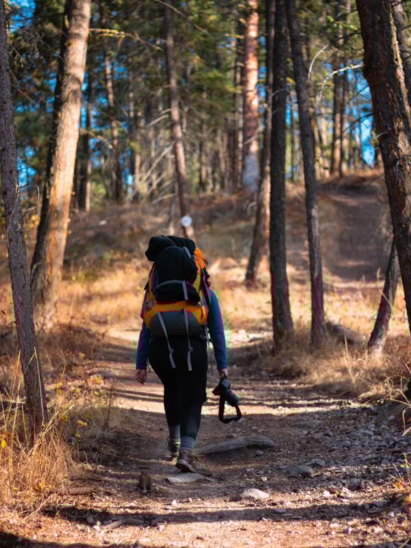 A woman with a heavy backpack hikes up a dirt trail at Spion Kop.