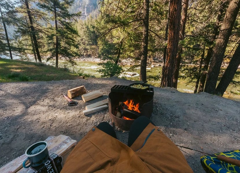 Woman sits near a campfire with the Similkameen River in the background