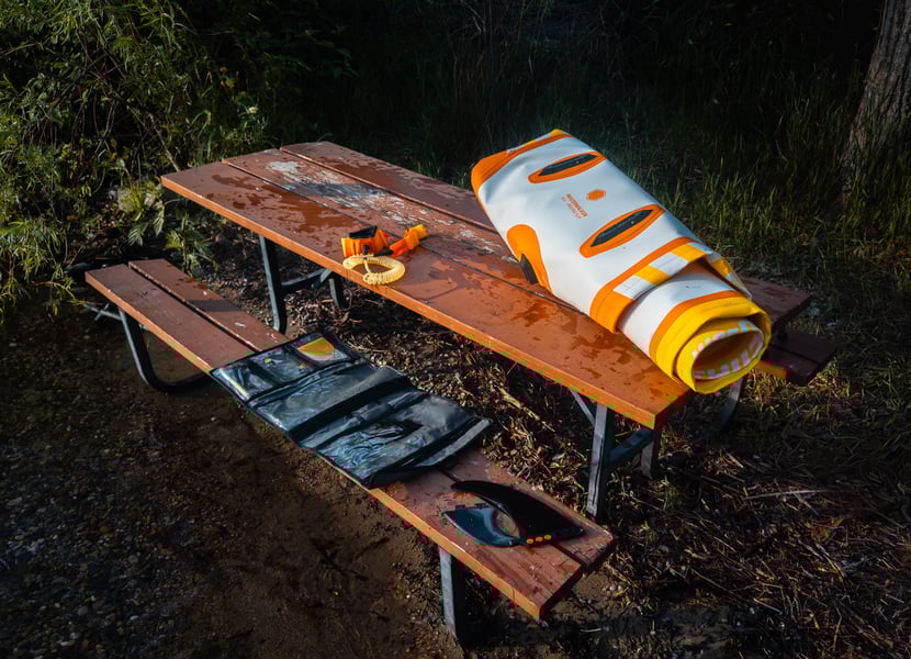 A rolled up paddleboard and accessories on a picnic table near the lake