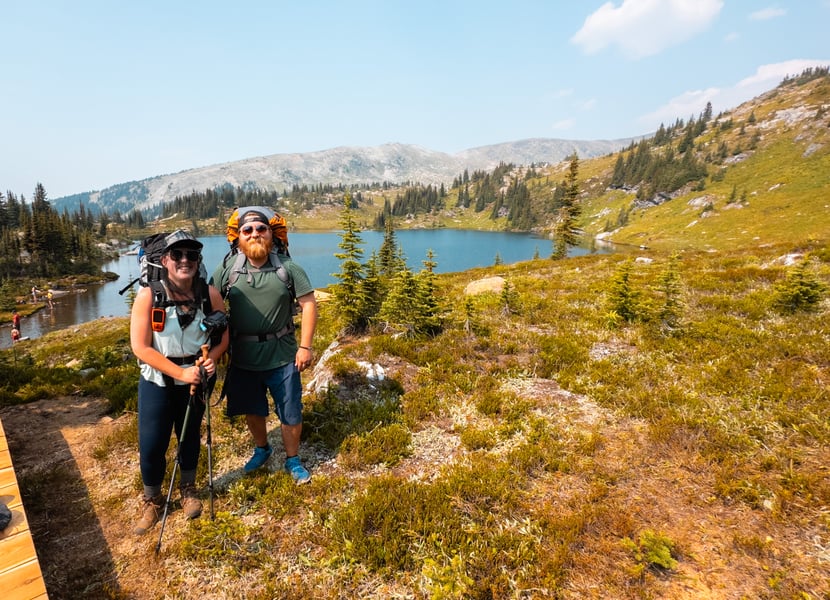 Man and woman backpacking with a beautiful lake behind them.