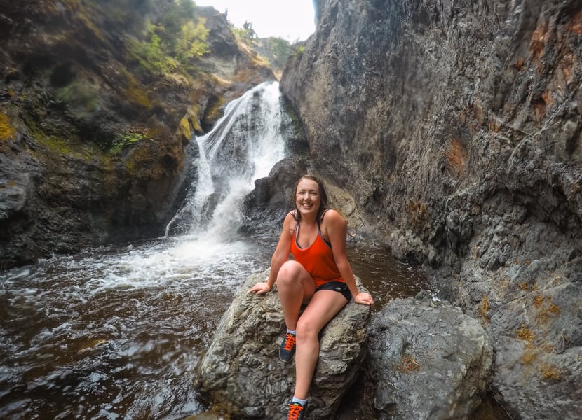Woman in red sits on a rock in front of a canyon waterfall.