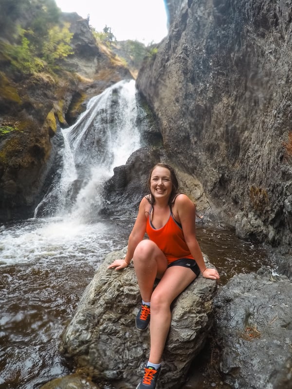 Woman in red sits in front of Bear Creek waterfall in Kelowna, BC