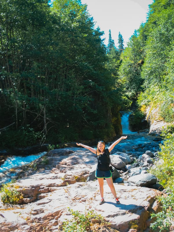 Woman standing in front of a waterfall cascading through Lava Canyon near Mount St. Helens, surrounded by volcanic rock