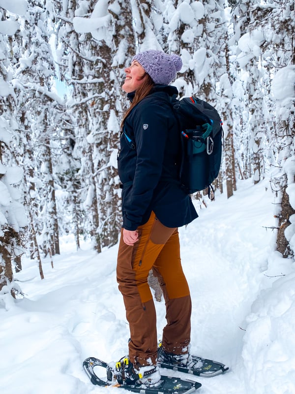 Woman in snowshoes. KUHL logo visible on the sleeve of the Voyagr rain jacket.