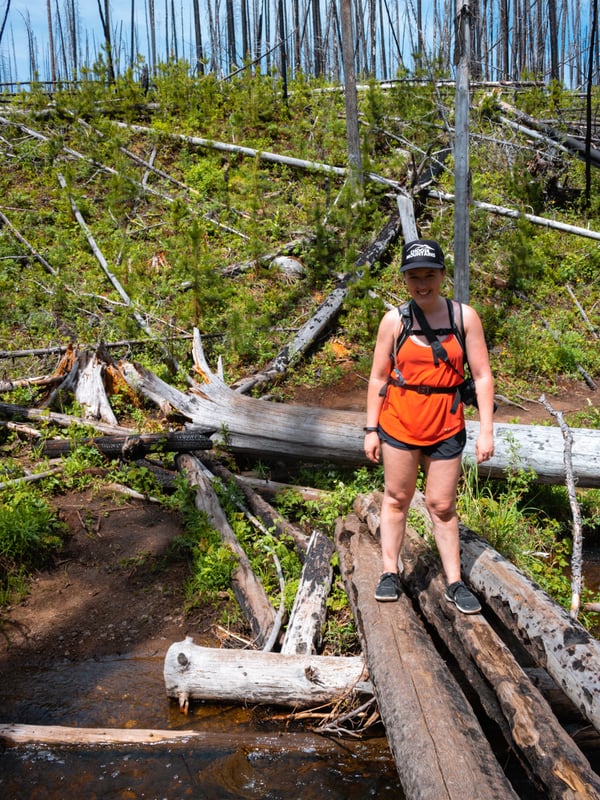 Woman crosses Christie Creek on a log.