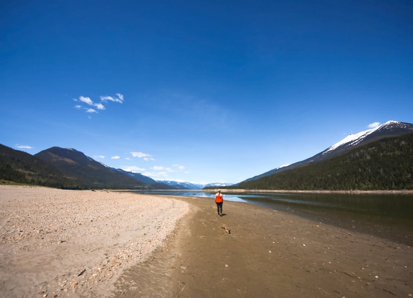 Woman walks down a large sandy beach in Revelstoke