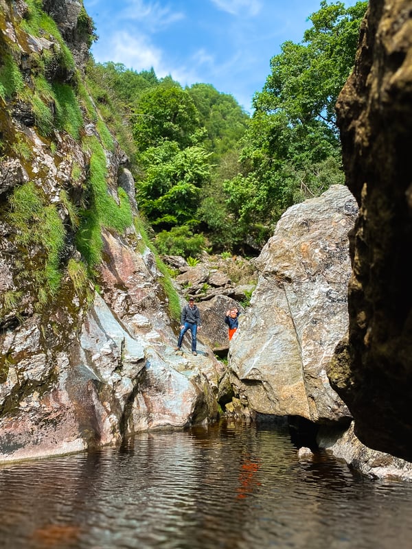 Two men at the far end of a pool surrounded by rocks.