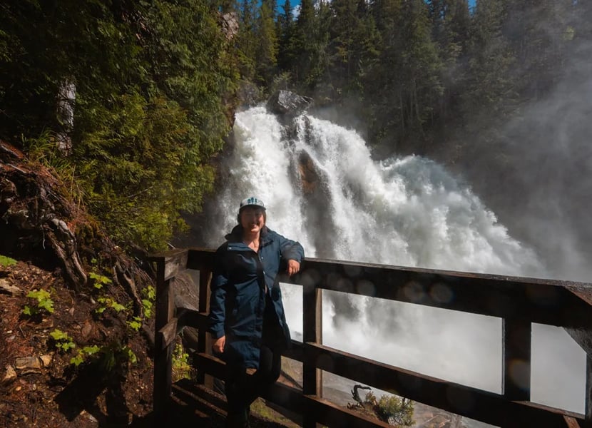 Woman wearing a hat and rain jacket stands in front of Rainbow Falls in the Monashee Mountains