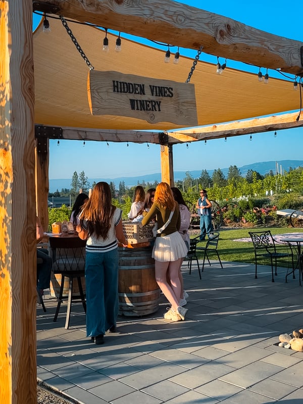 Group of women doing a wine tasting under a canopy. A sign at the front says "Hidden Vines Winery"