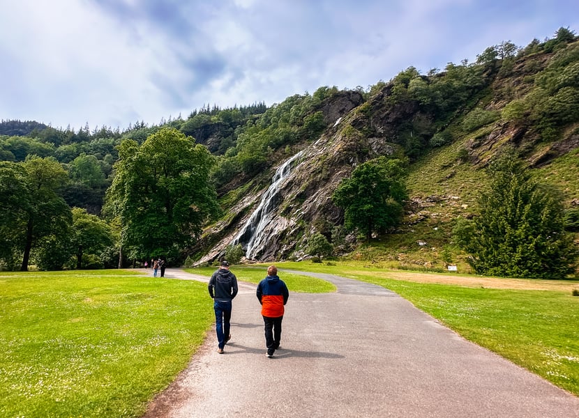 Two men walking on a paved trail towards Powerscourt Waterfall.